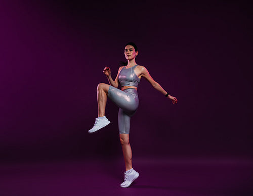 Full length of young slim female in silver sportswear warming up on magenta backdrop