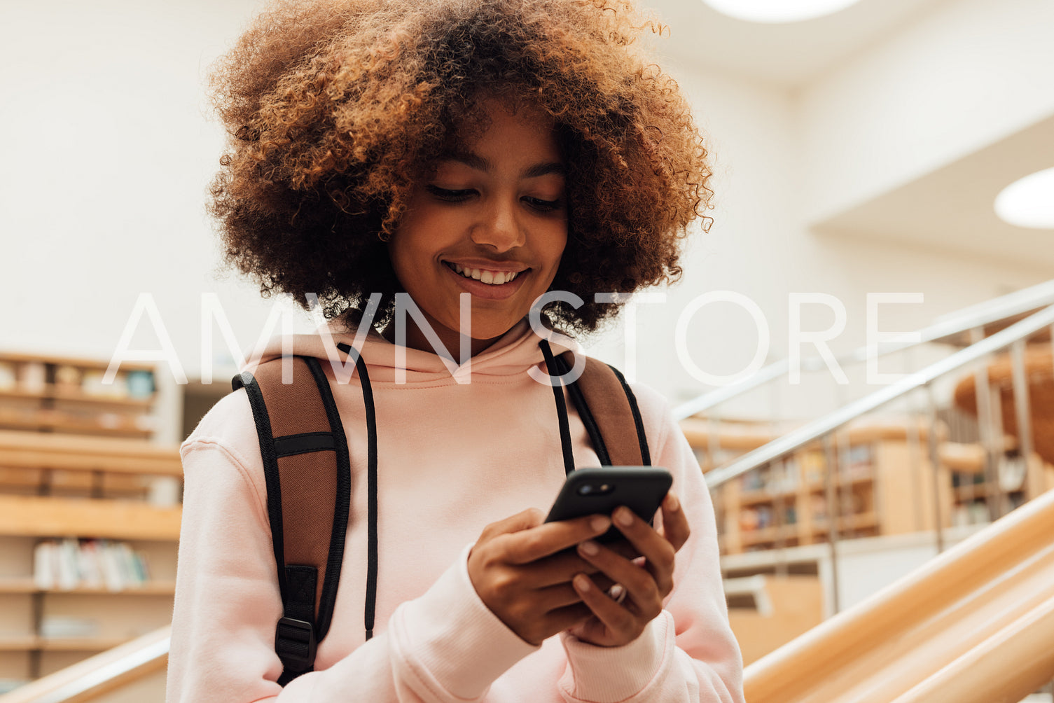 Smiling girl holding smartphone in high school library