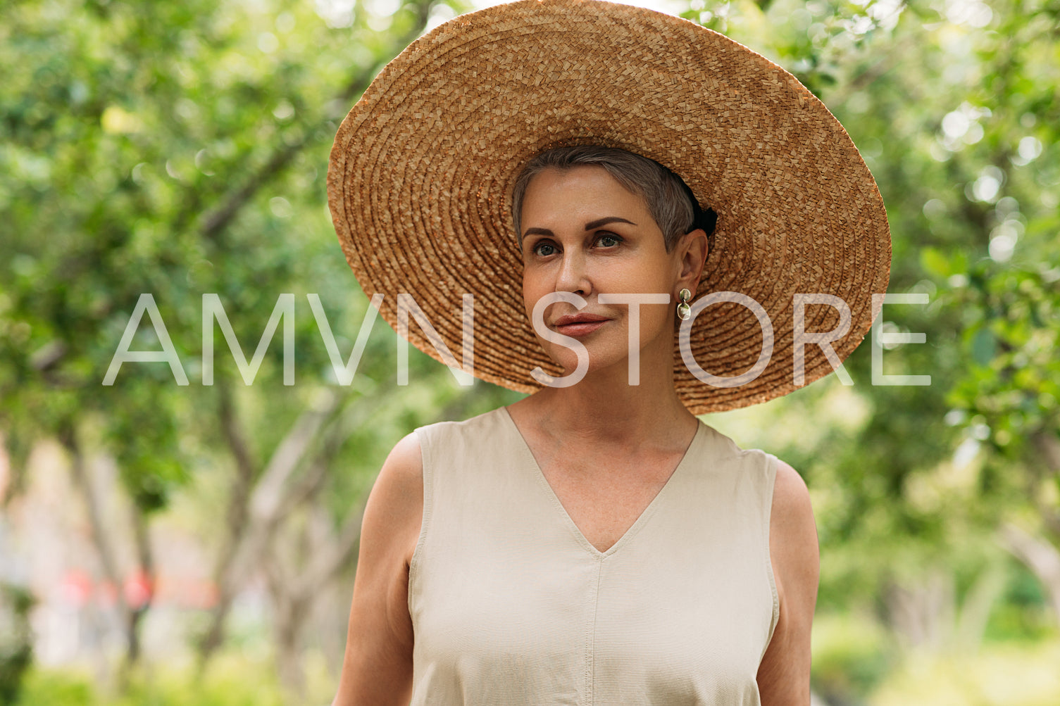 Portrait of an aged female in a big straw hat looking away while standing outdoors