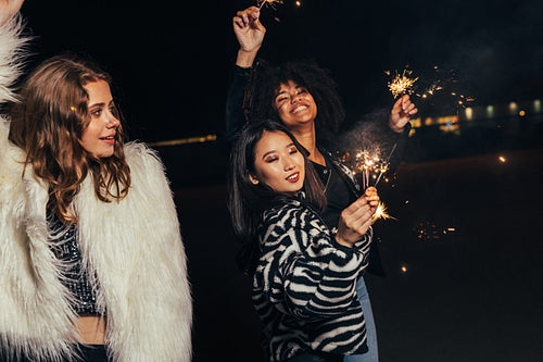 Group of multi ethnic girls with sparklers walking on street at night