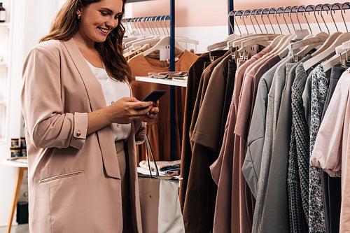 Smiling woman using cell phone while standing at a rack in a clo