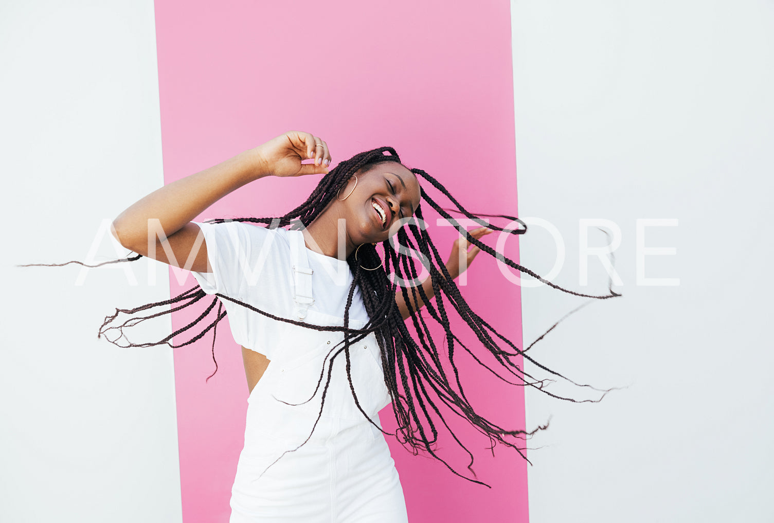 Playful woman with long braided hair dancing at a white wall with pink stripe