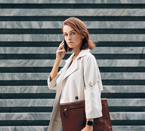 Confident businesswoman in coat talking on the mobile phone looking away