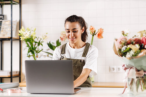 Woman wearing apron standing at the counter and working on laptop computer in a flower shop