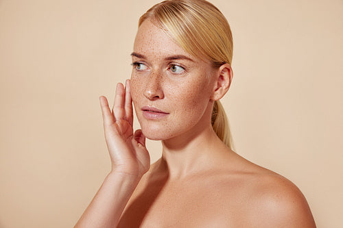 Studio shot of a young woman with freckles touching her face