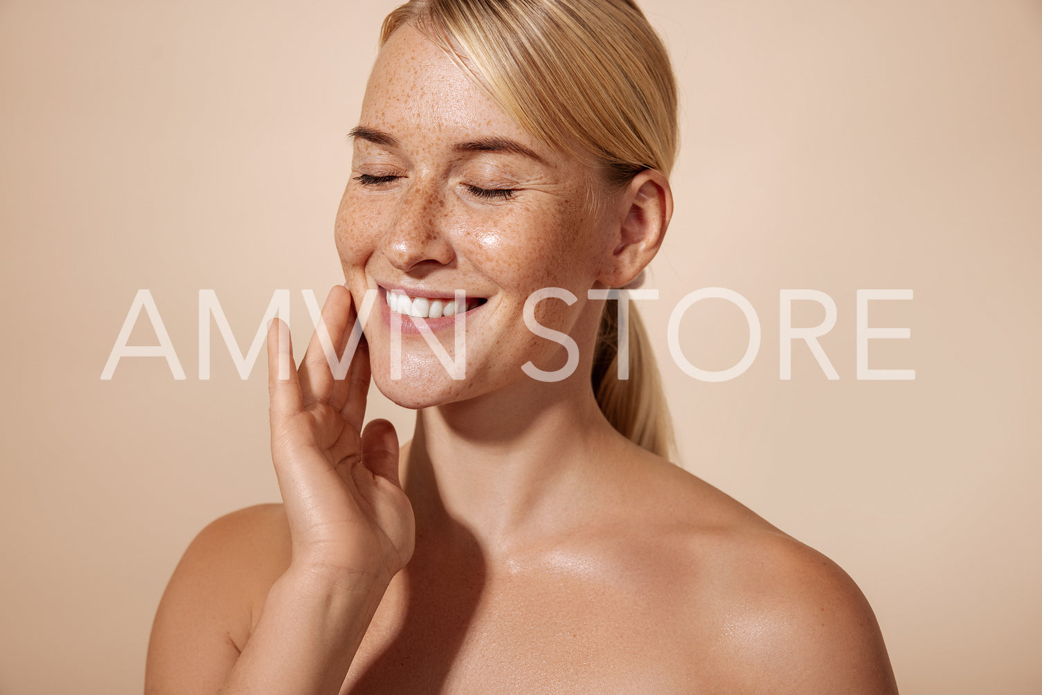 Cheerful female with blond hair massaging her cheek in studio against pastel background