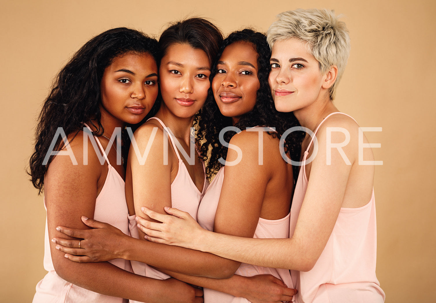 Four beautiful women hugging each other in a studio. Diverse females standing at background.	