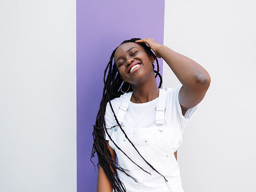 Young woman with braids having fun outdoors. Happy female with closed eyes wearing white casual clothes.