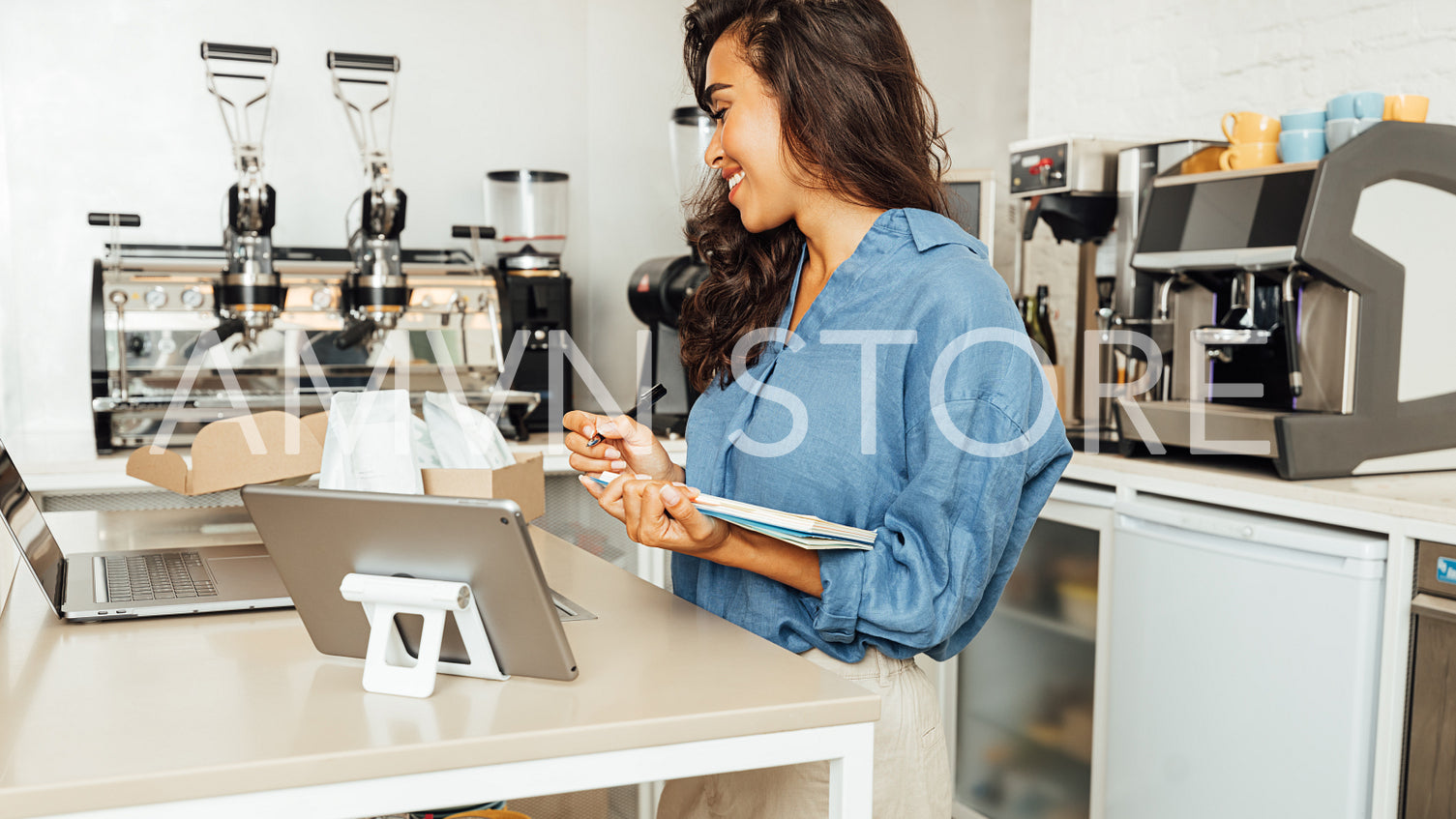 Side view of businesswoman in casuals standing in her coffee shop and making an accounting of goods.	