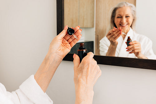 Close up of a senior woman's hands holding a dropper and a bottle with a liquid facial treatment in bathroom