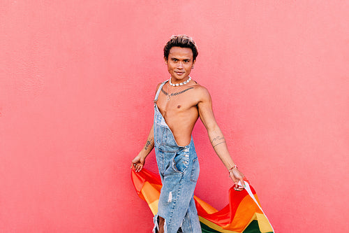 Young man walking with rainbow flag against pink wall