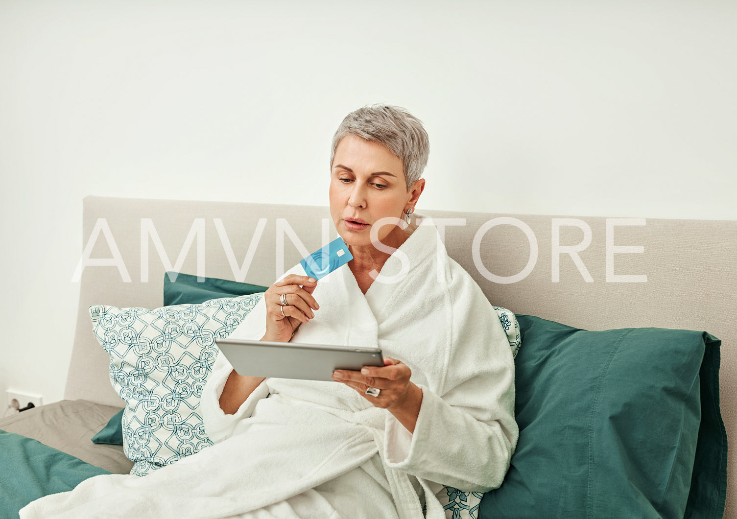 Senior woman shopping online while lying on a bed in hotel room