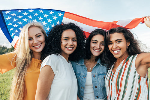 Group of young multi-ethnic women holding American flag celebrating 4th of July