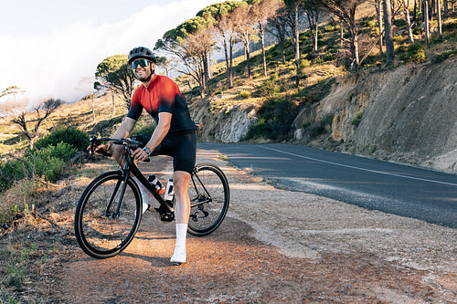 Smiling cyclist standing on a roadside in wild terrain. Male bike rider standing with his bicycle at taking a break.