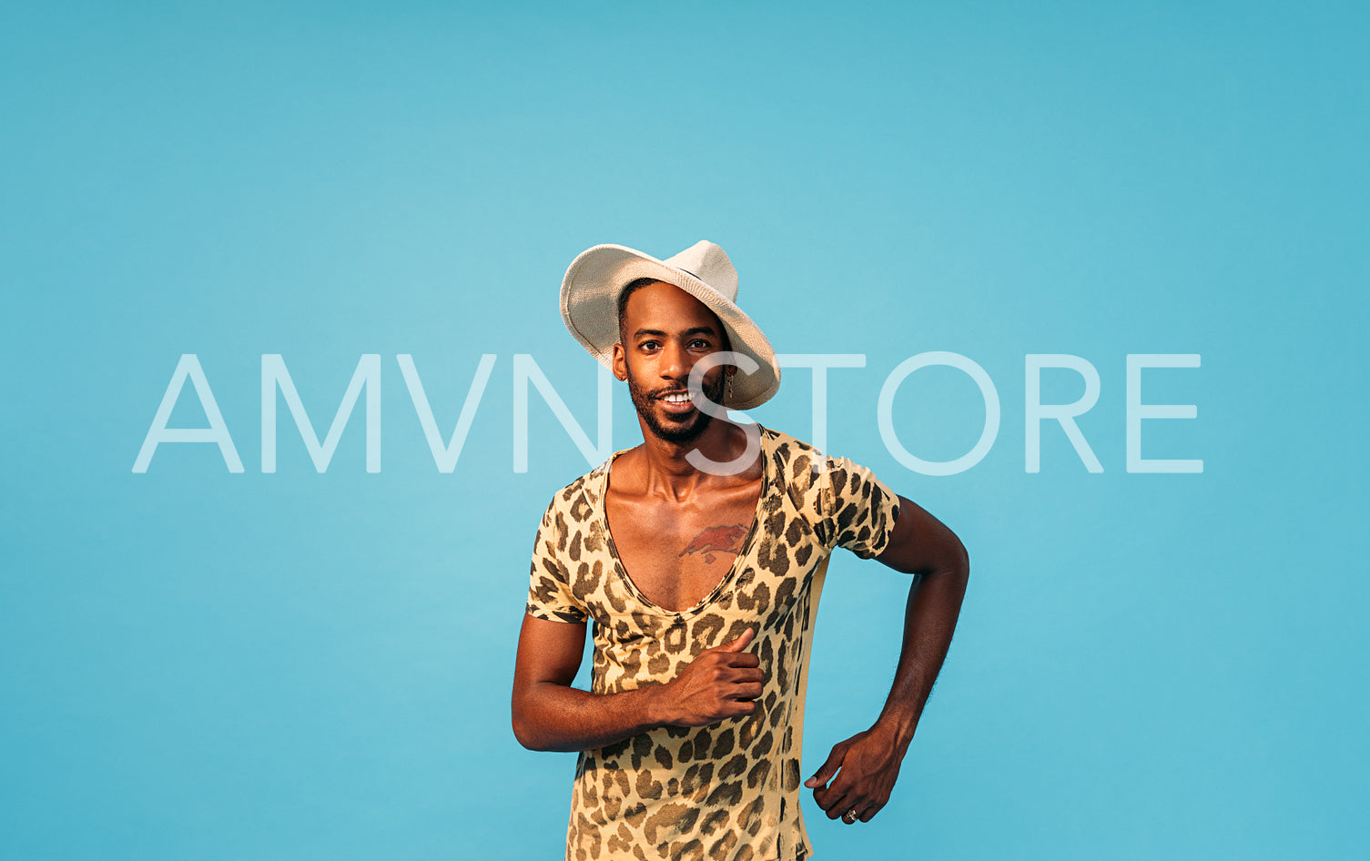 Stylish man in straw hat dancing in studio and looking at camera against blue background 