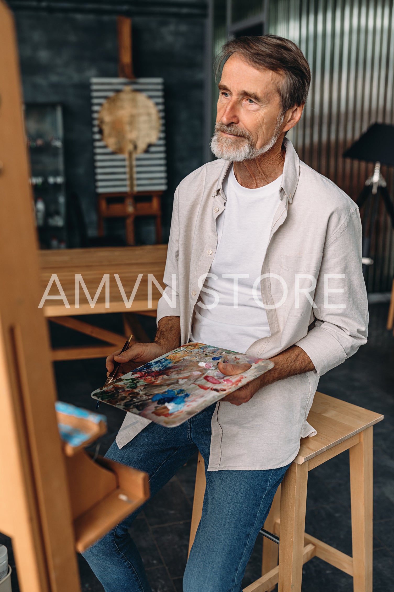 Bearded artist sitting in front of easel, getting ready to paint	