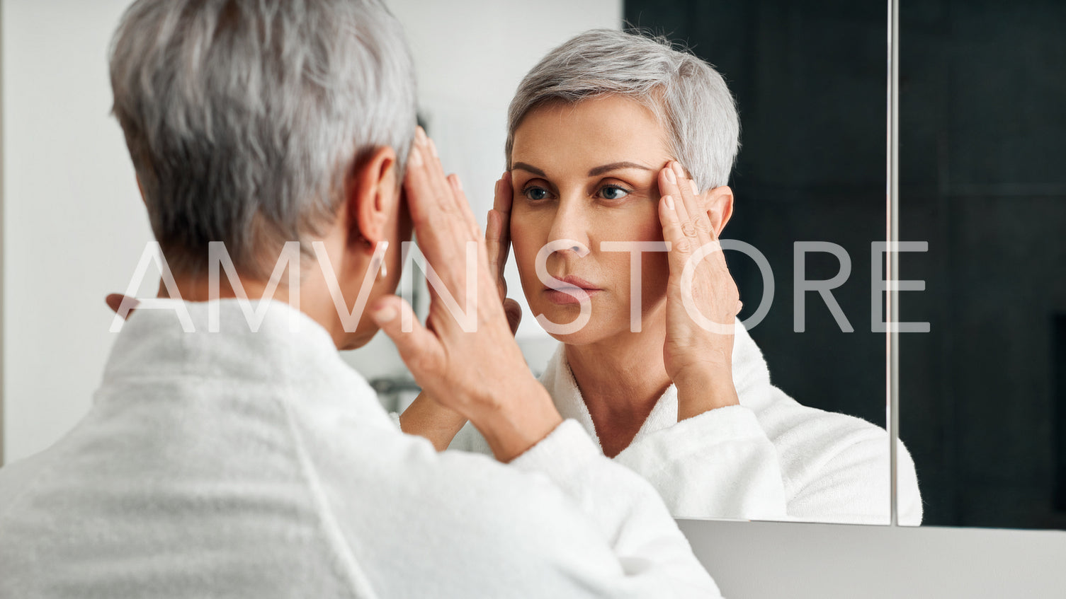 Mature woman in a bathroom in front of a mirror touching head with hands