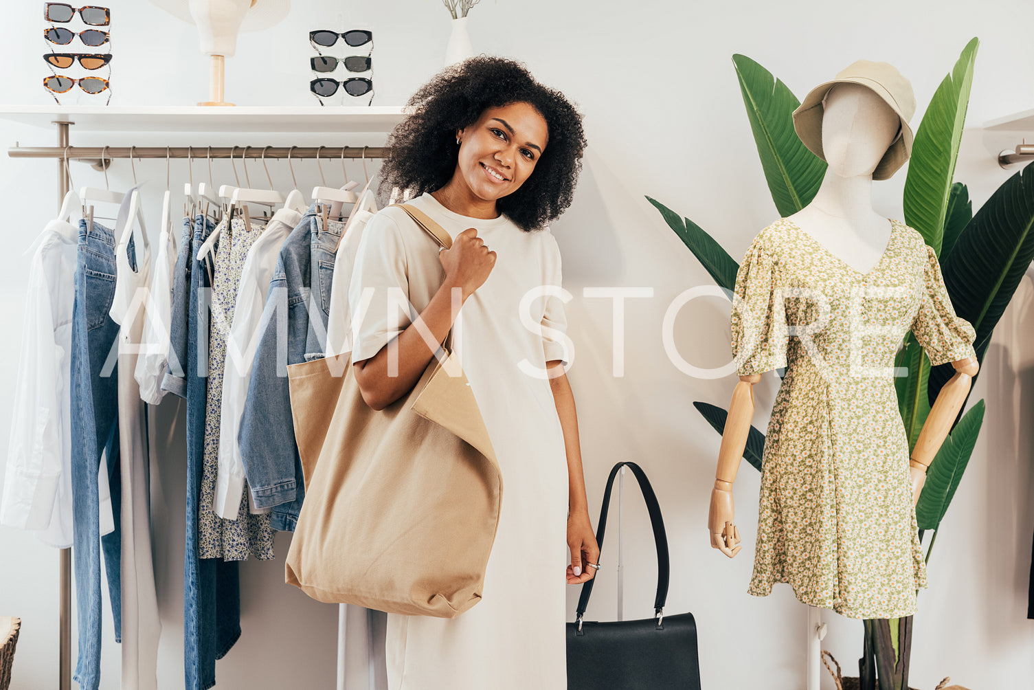 Beautiful stylish woman with shopping bag standing in boutique at a rack and looking at camera