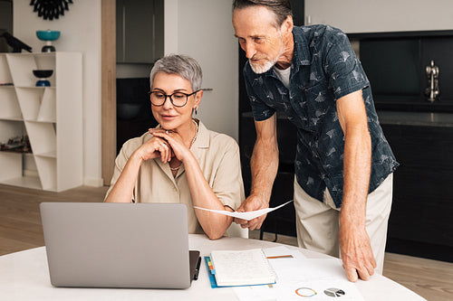 Senior caucasian couple calculating bills at home. Two mature people looking at laptop and managing finances.