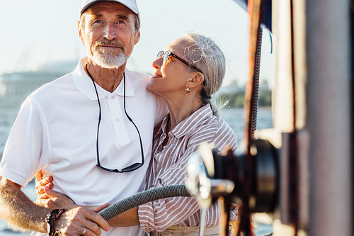 Mature woman looking and embracing on her husband while he steering a sailboat