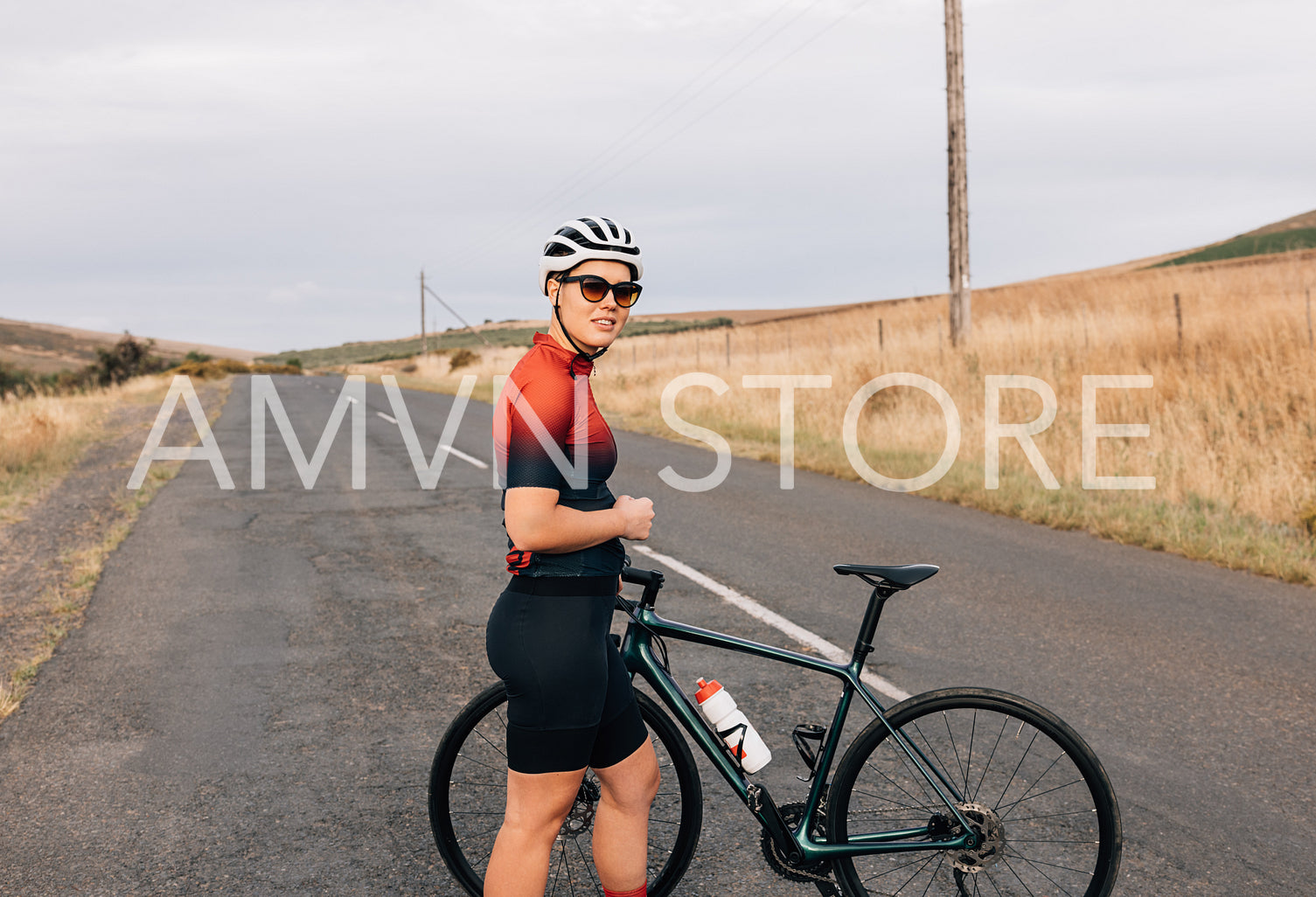 Woman cyclist in sportswear standing with her bike on countryside road looking away 