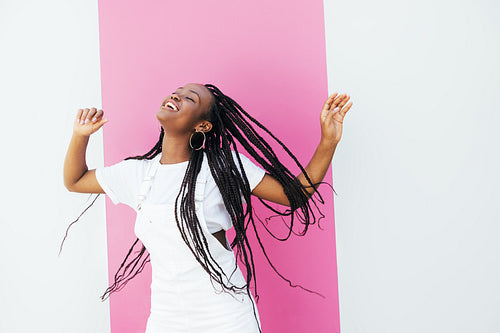 Happy girl in white clothes dancing and having fun at white wall with pink stripe