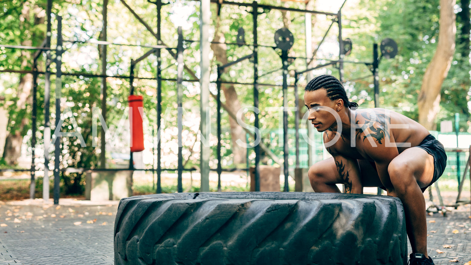 Side view of a bare-chested athlete doing squats with huge tire on sports ground outdoors