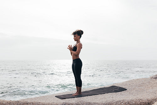 Full length of a slim female standing with folded hands on mat outdoors