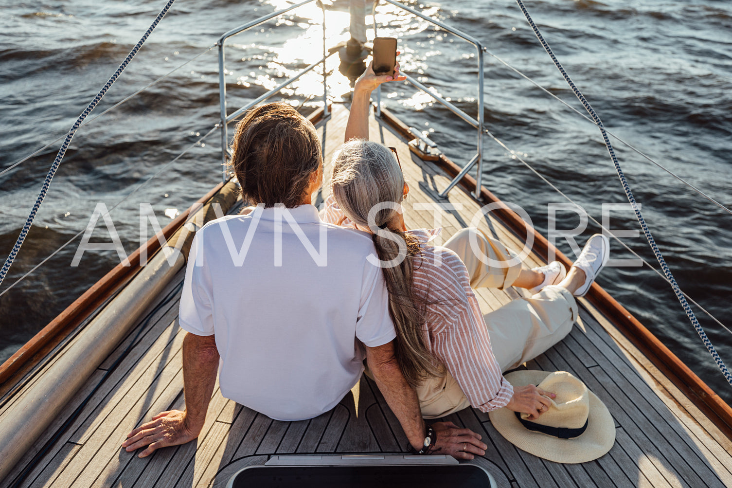 Rear view of senior man and woman sitting on private yacht and taking selfie with mobile phone	