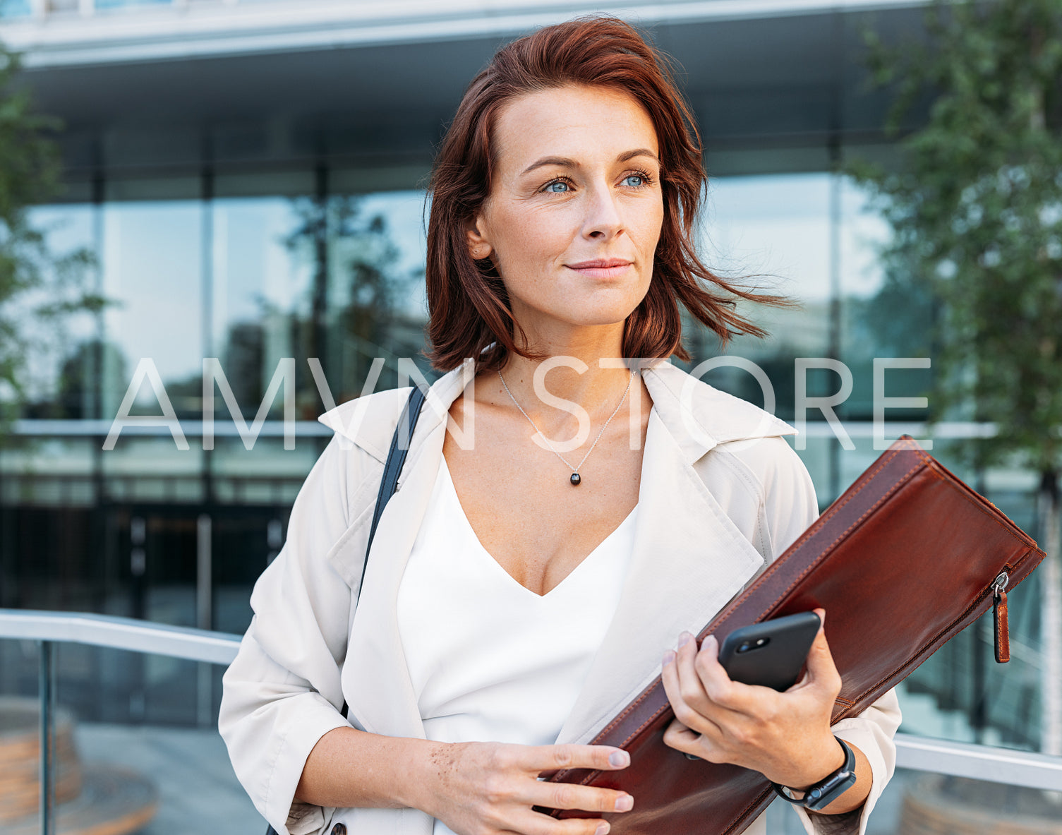 Portrait of a middle-aged attorney. Businesswoman with ginger hair holding a leather folder standing outdoors looking away.