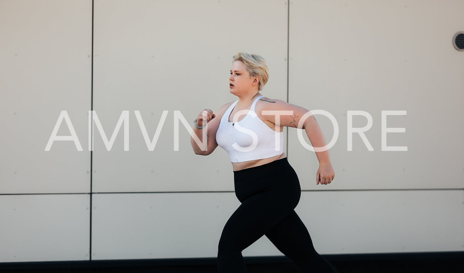 Young woman with short hair running outdoors at wall. Female with plus size body jogging on roof.	