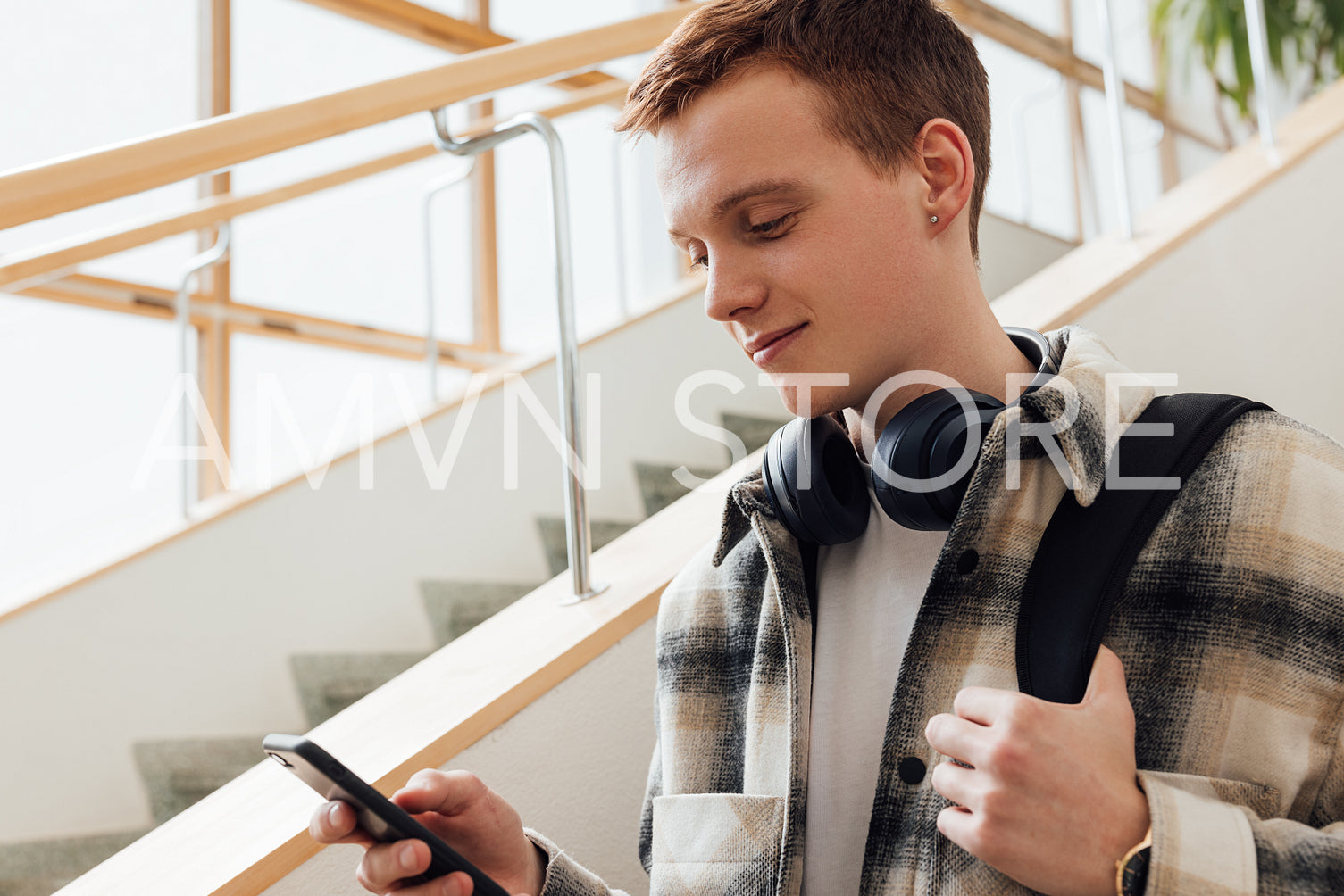 University student looking at his smartphone while standing at staircase