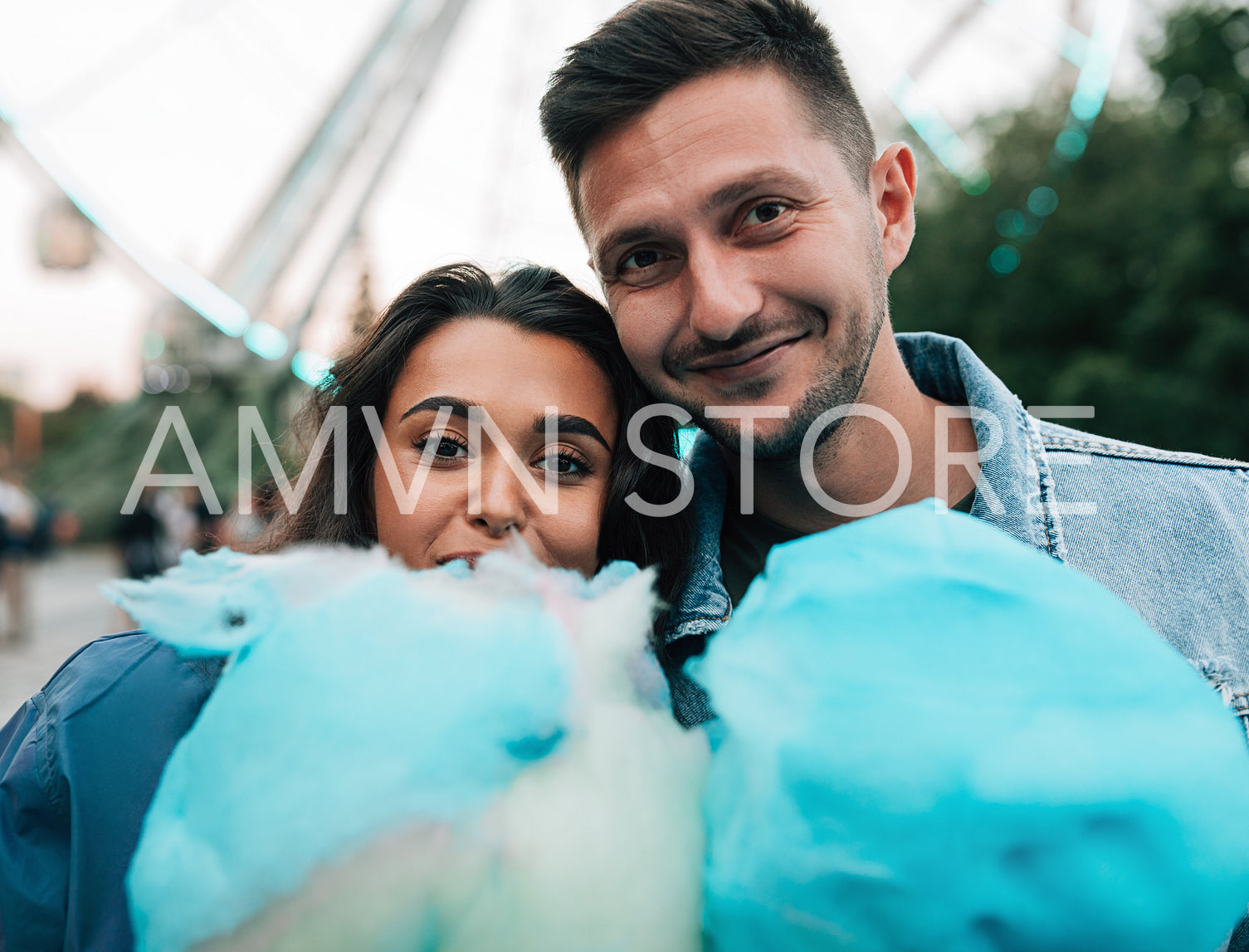 Portrait of a young couple looking at the camera holding a blue cotton candy