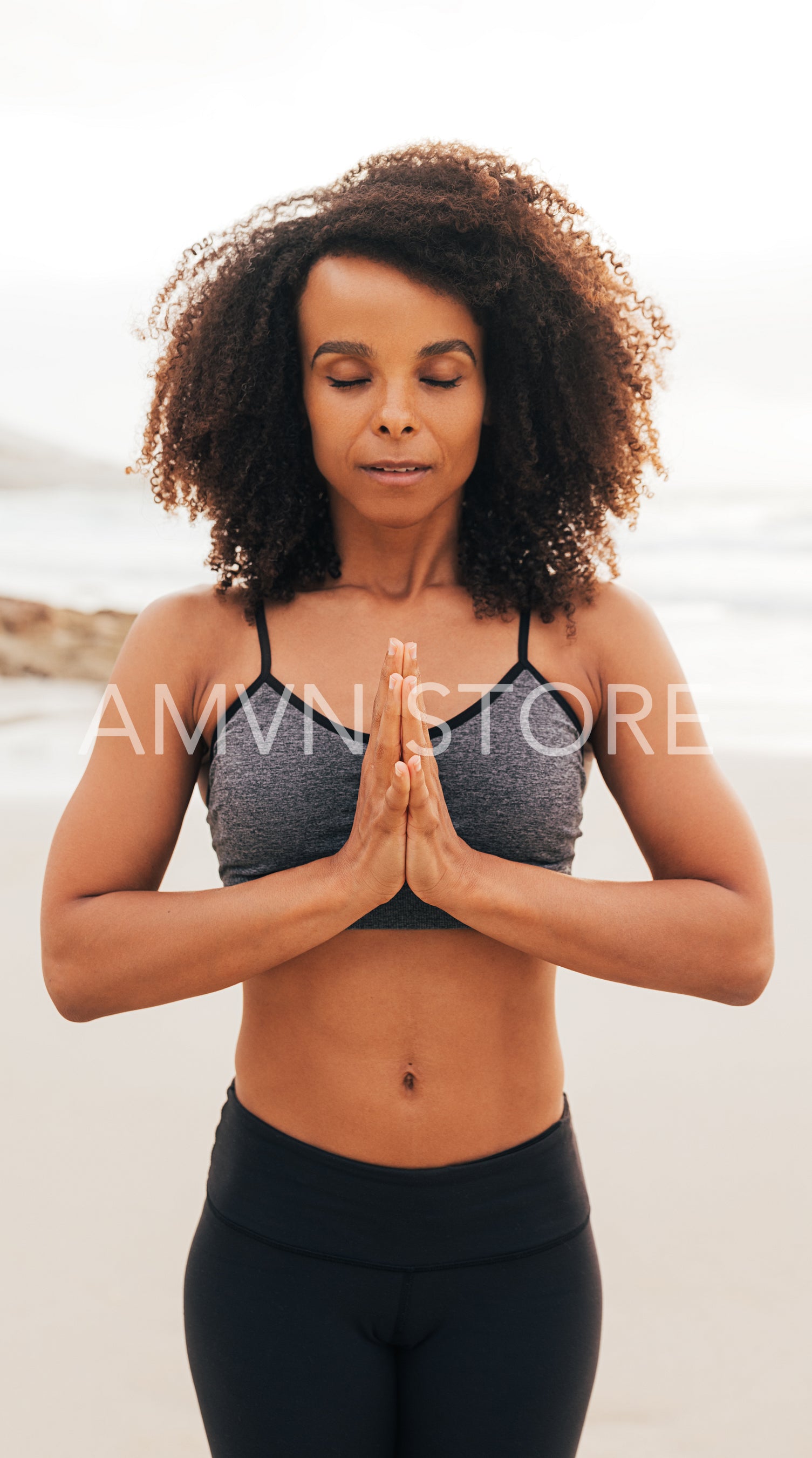 Woman with closed eyes and folded hands standing on a beach and meditating