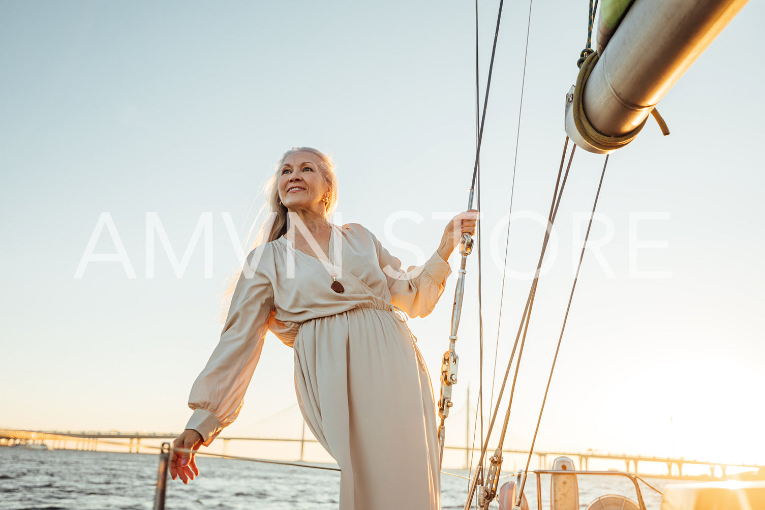 Portrait of mature woman in dress standing on yacht at sunset. Beautiful senior woman holding a rope and looking away.	