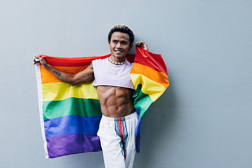 Smiling handsome guy holding rainbow flag outdoors