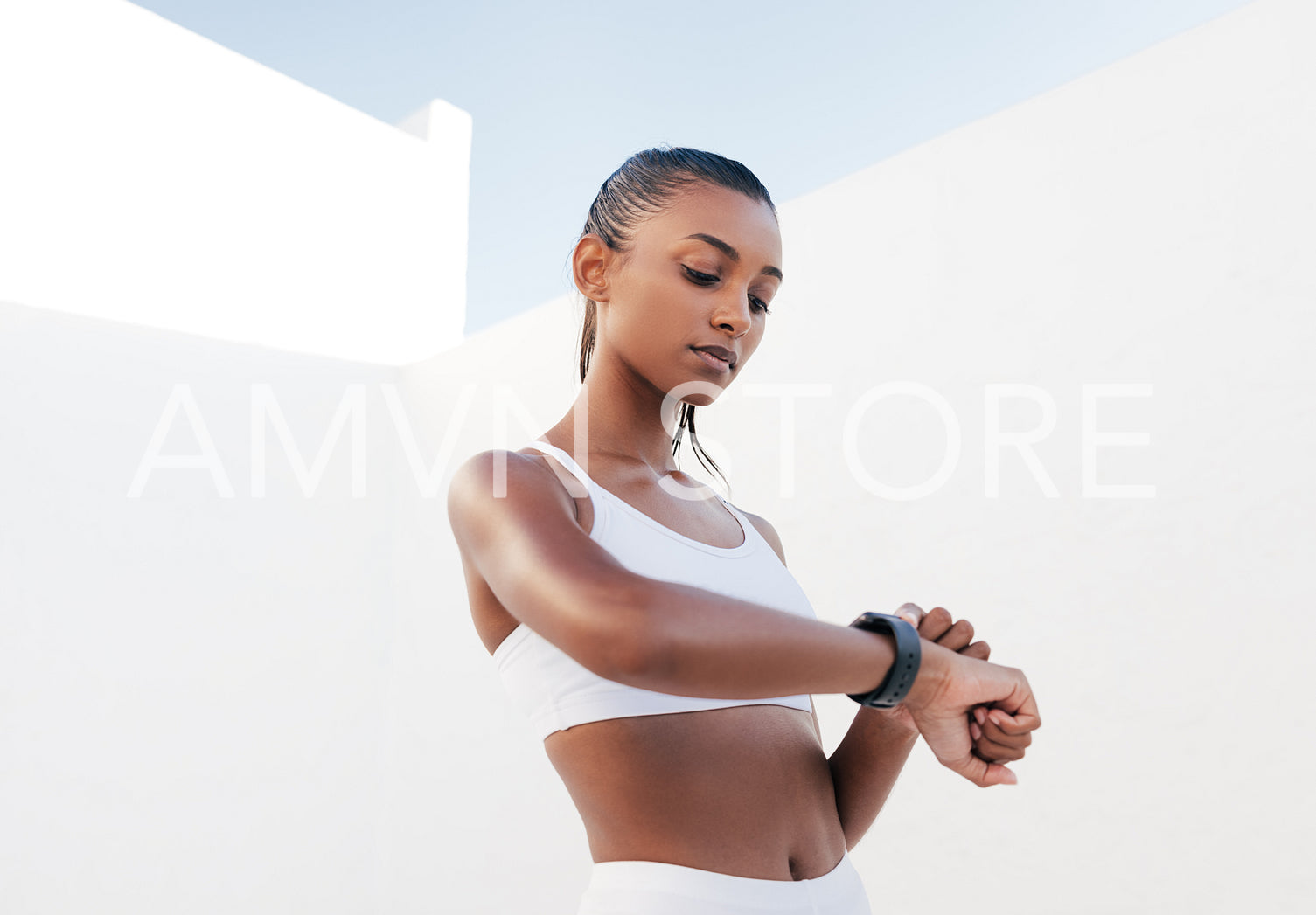 Confident female athlete checking her pulse. Healthy woman in a white sports bra looking on smartwatch.