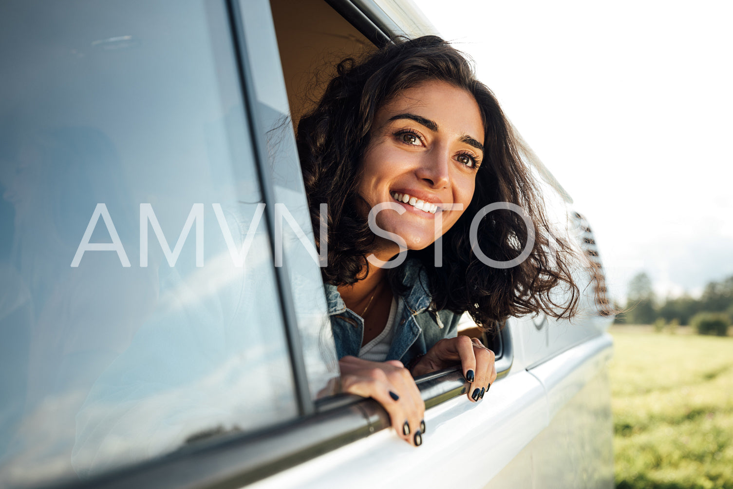 Beautiful brunette looks out of a window enjoying a road trip. Young woman in camper van looking into a distance.