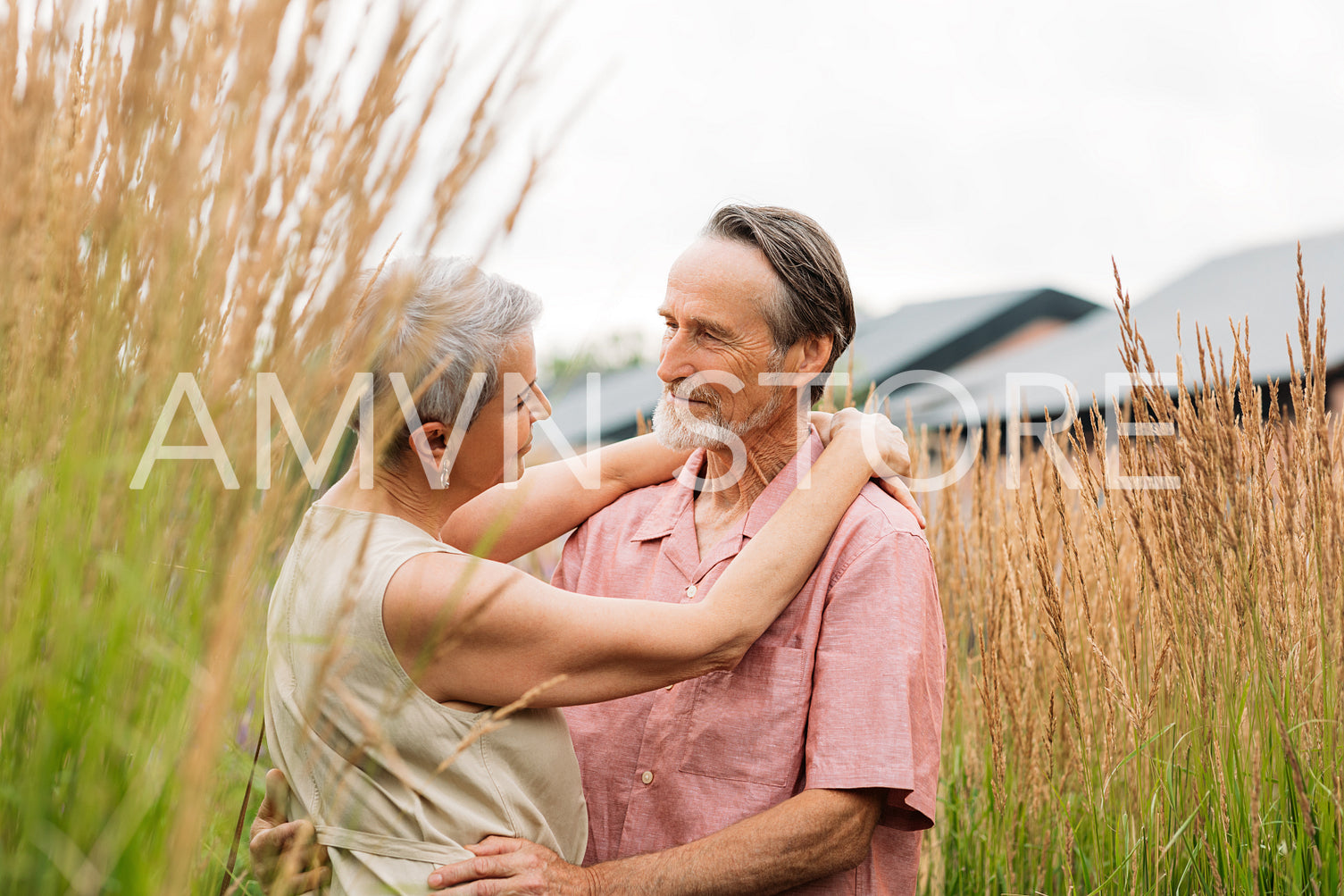 Mature couple in casuals looking at each other and hugging while standing on a wheat field