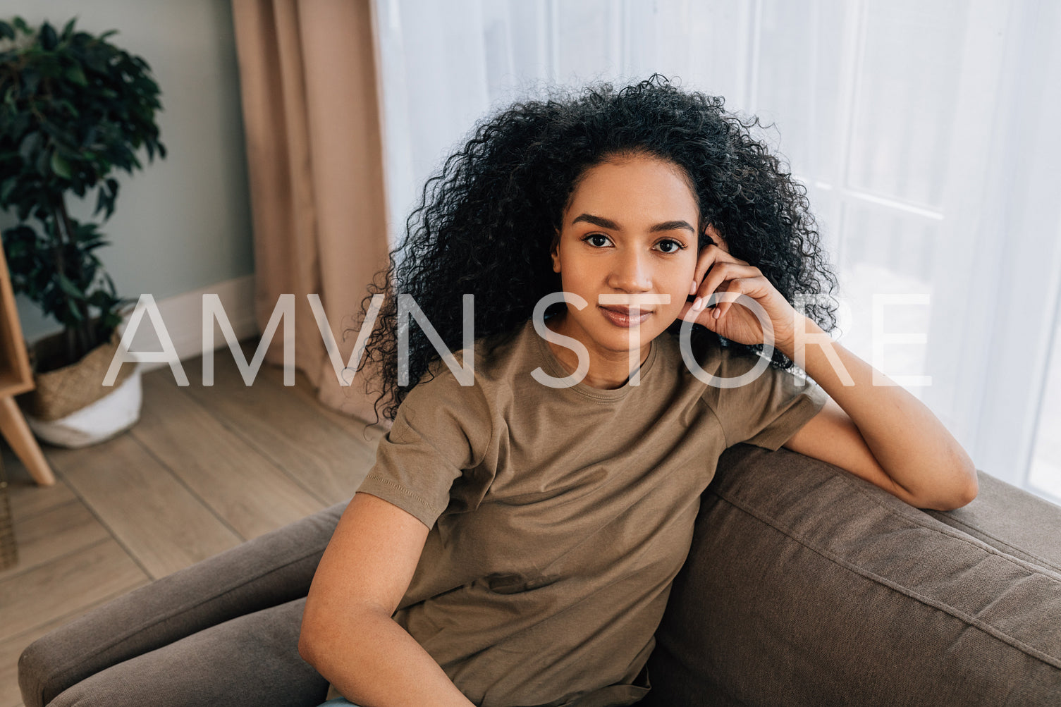 Portrait of a beautiful woman with black curly hair sitting on couch in living room	