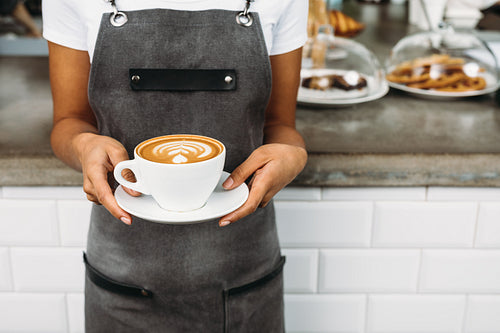 Unrecognizable waitress holding a cup of latte with rosetta in cafe