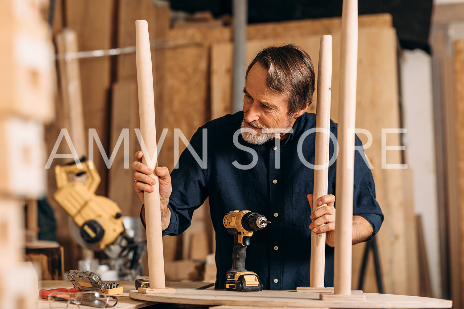 Senior man observing table legs in the workshop. Carpenter working on furniture.	