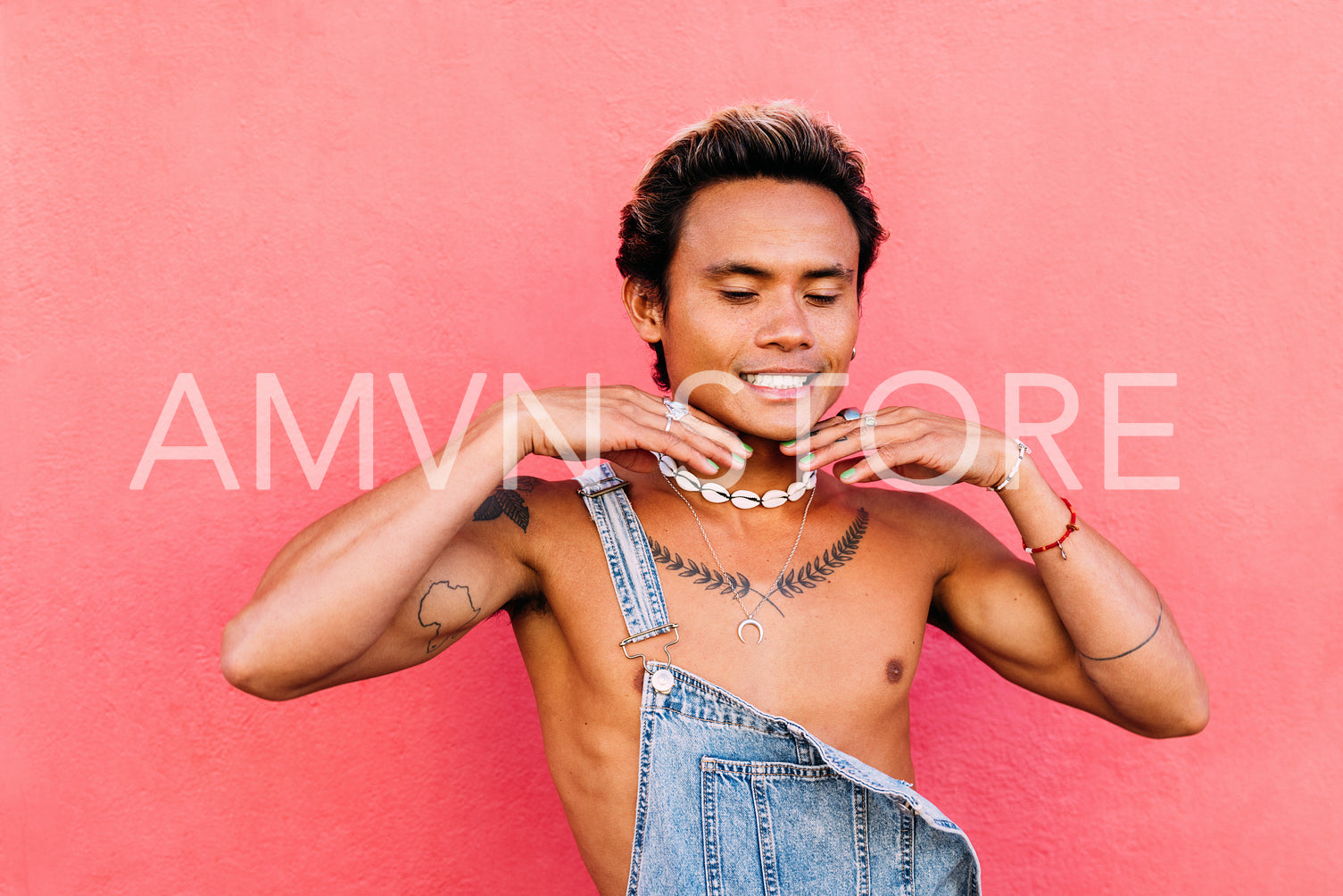 Portrait of a young smiling guy having fun with closed eyes while standing at pink wall