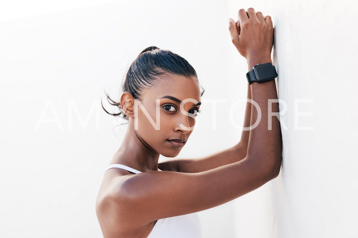 Portrait of a beautiful sportswoman leaning white wall outdoors. Young female relaxing and looking at camera.