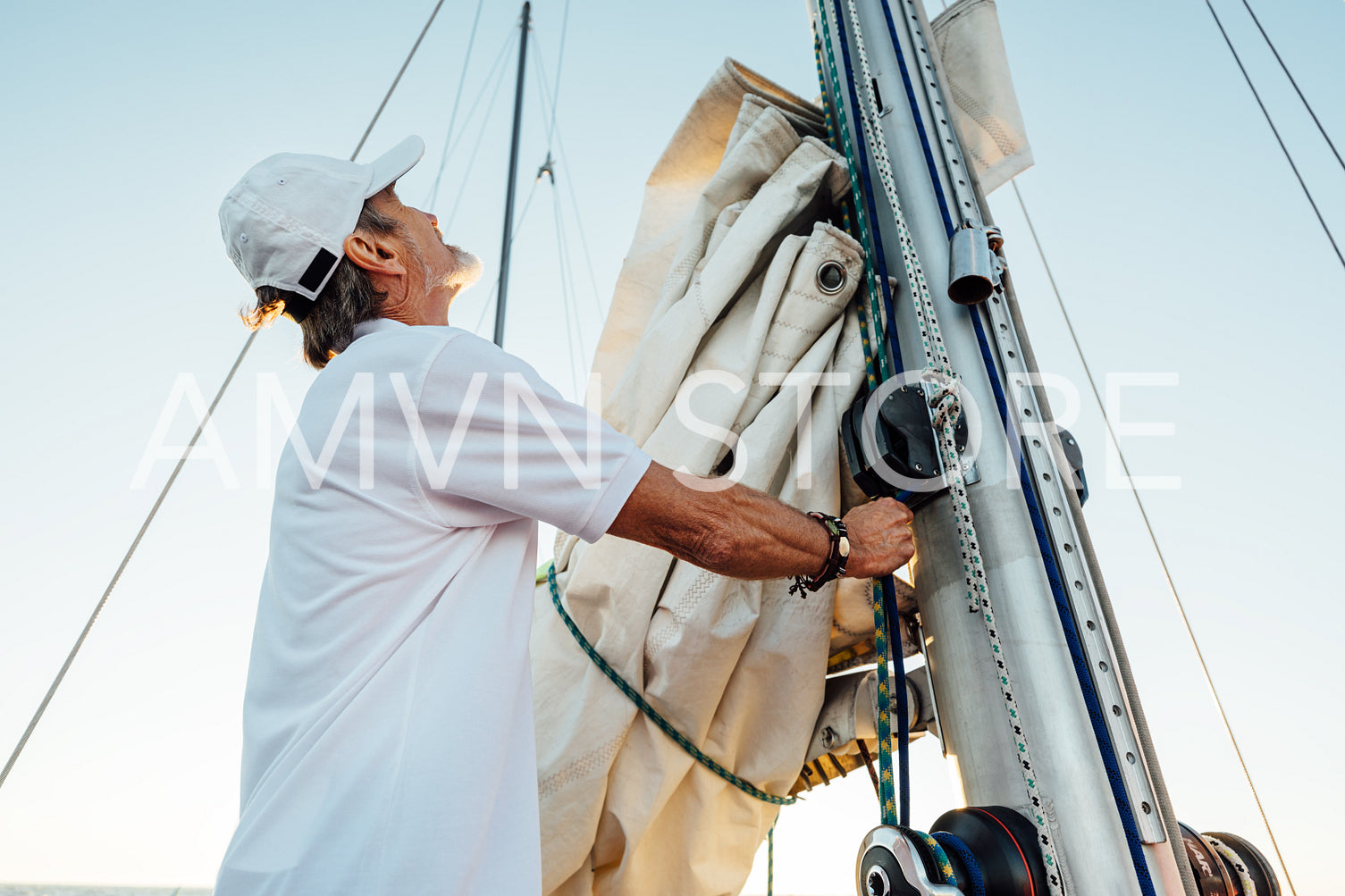 Mature captain looking up while adjusting sail. Senior yachtsman preparing a boat for a vacation trip.	