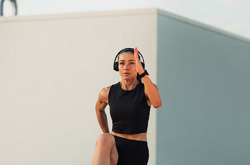 Young slim woman wearing headphones doing warming up exercises