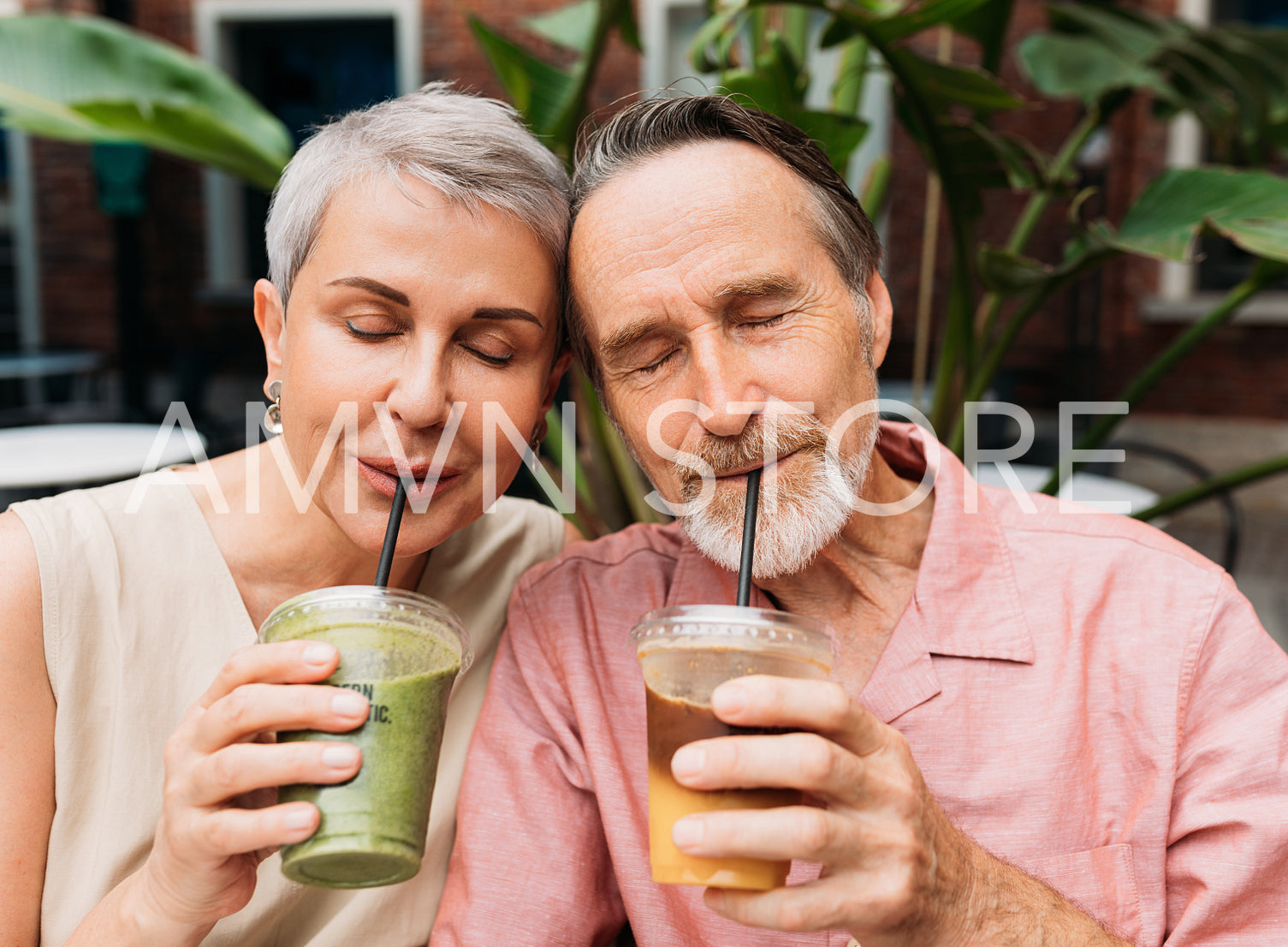 Mature couple drinking a smoothie. Wife and husband drink cocktails while sitting head to head with closed eyes.