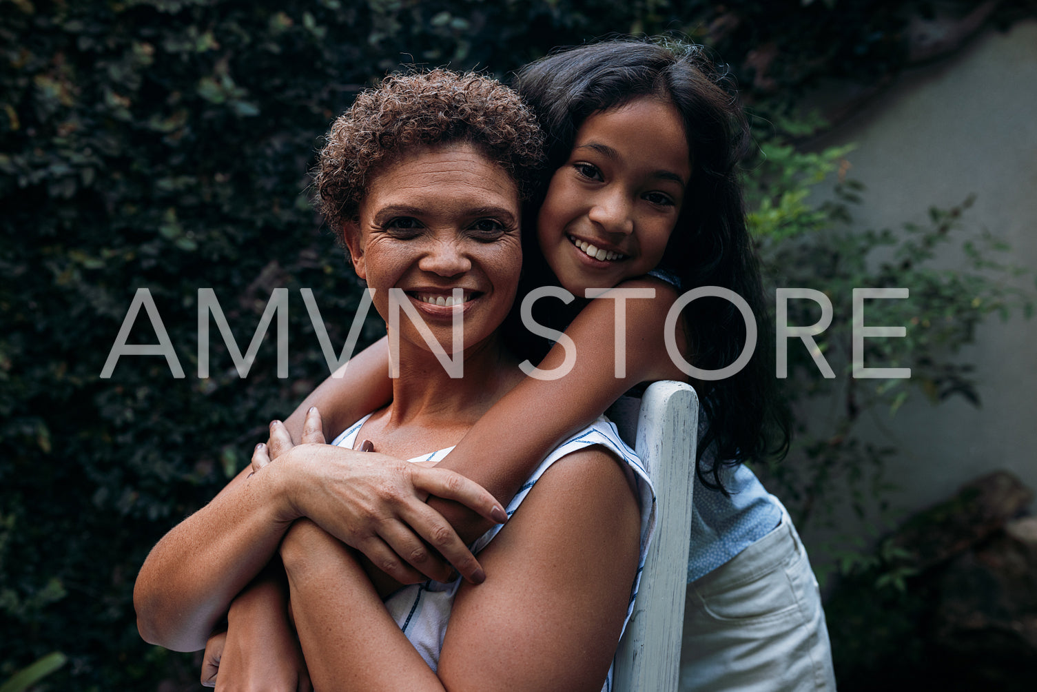 Portrait of a girl and her grandmother. Granny sitting on a chair granddaughter hugging her from back.