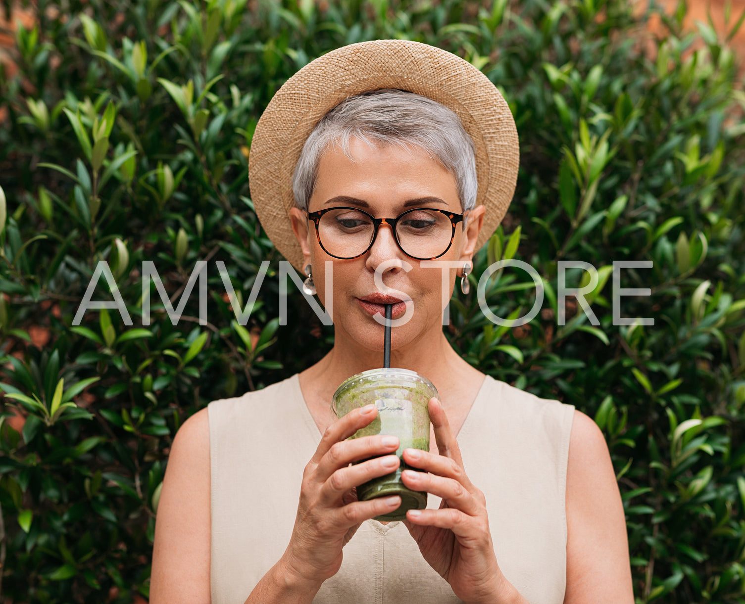 Aged woman with short hair drinking a smoothie. Senior female enjoying cocktail outdoors.