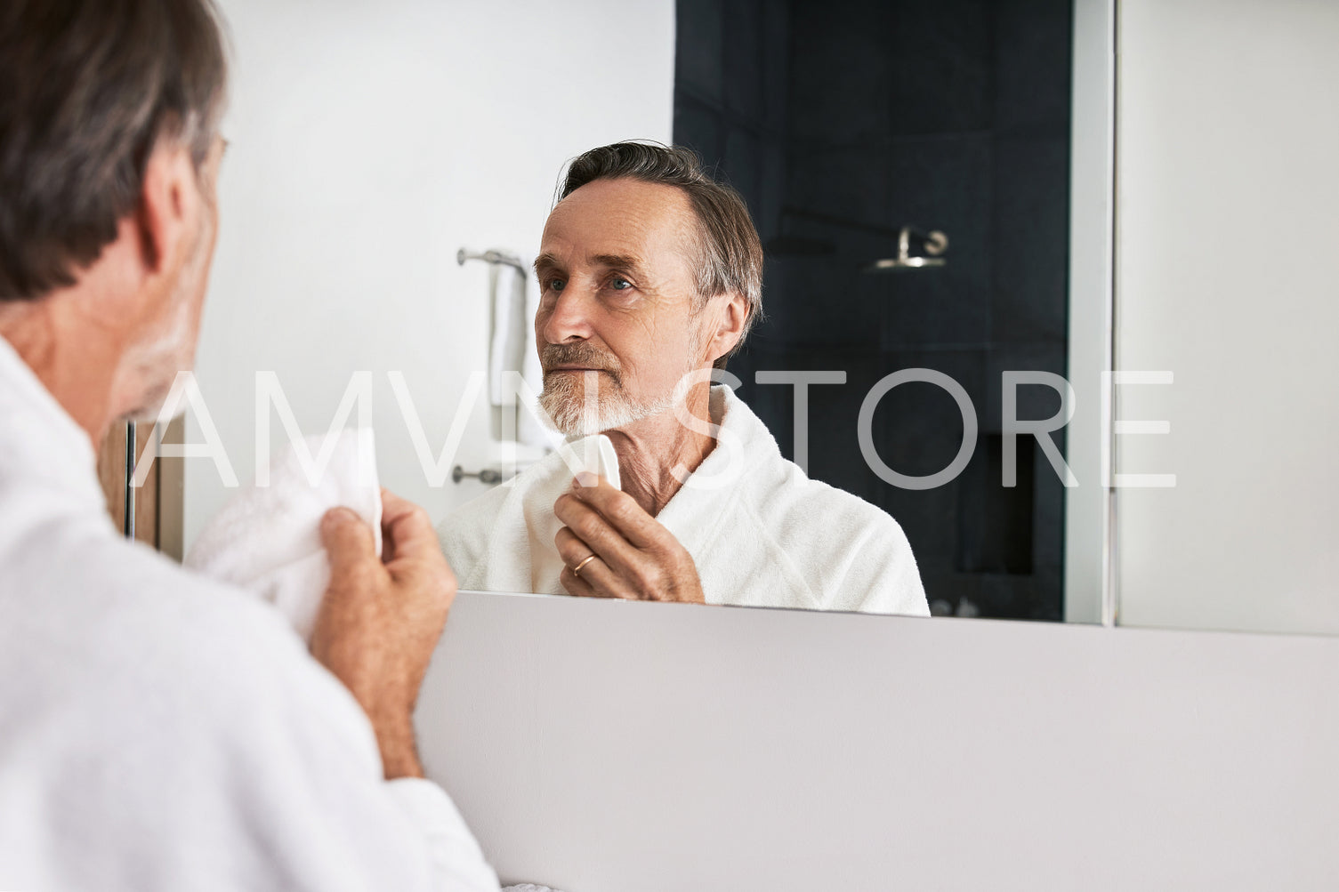 Mature man with beard holding a white towel doing morning skincare routine in the bathroom